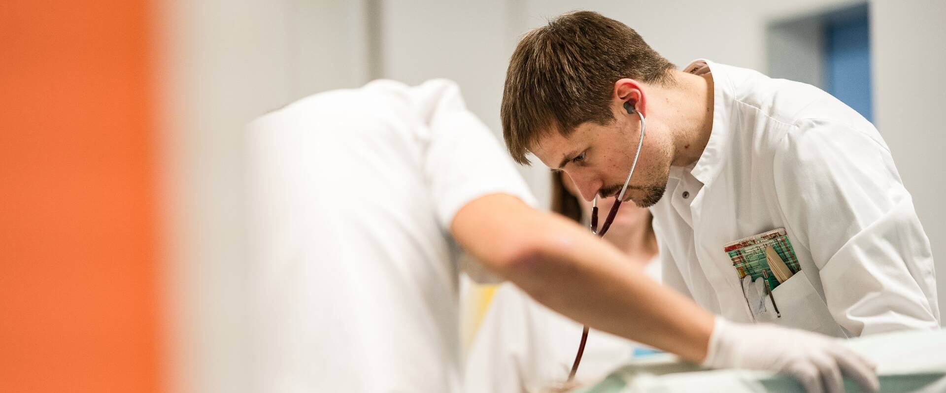Arzt mit Stethoskop beugt sich über Patient in Notaufnahme-Raum