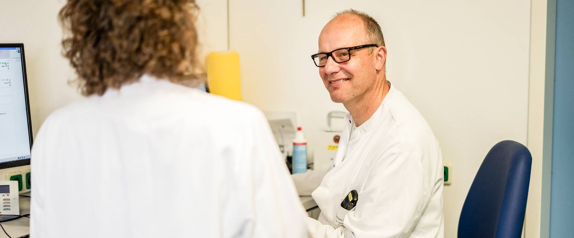 Arzt sitzend unterhält sich lächelnd mit Mitarbeiterin